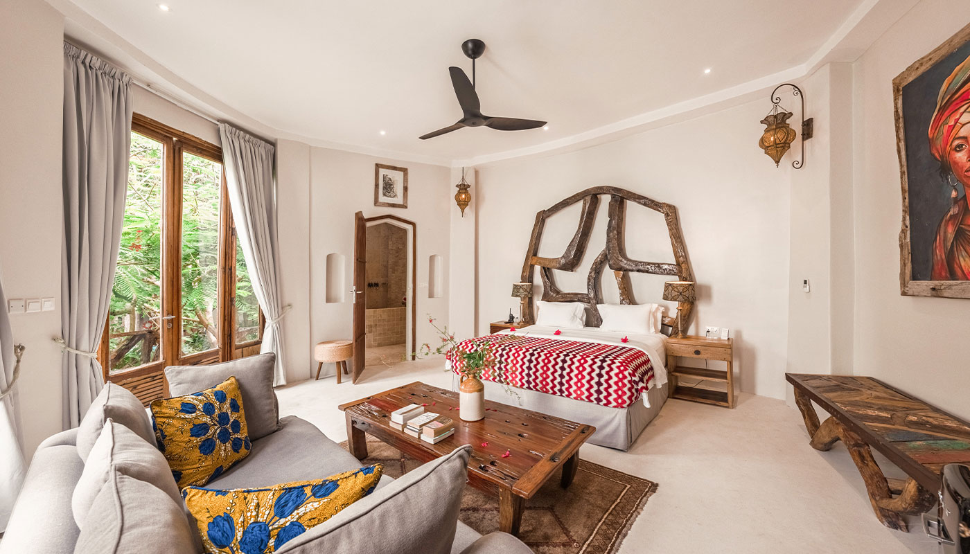 Spacious bedroom in Villa Korongo with a carved wood bed, seating area and garden-facing windows