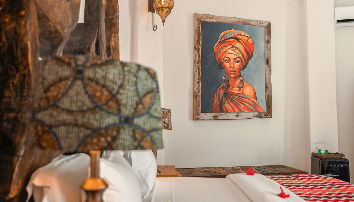 Framed portrait above a bed in Villa Korongo, with a patterned lamp in the foreground