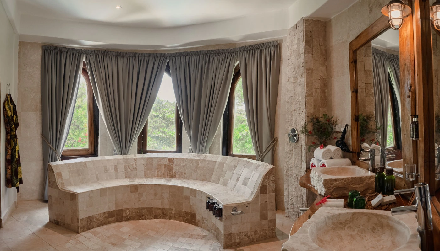 Elegant bathroom at Mbingu Villa in Xanadu Luxury Villas & Retreat, Zanzibar, featuring a curved natural stone bench, large mirrors and stylish stone washbasins.
