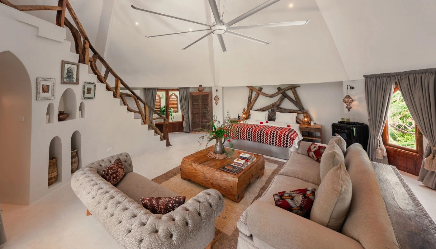 Spacious bedroom and living area at Mbingu Villa in Xanadu Luxury Villas & Retreat, Zanzibar, featuring an elegant double bed, a comfortable seating area and natural wooden accents.