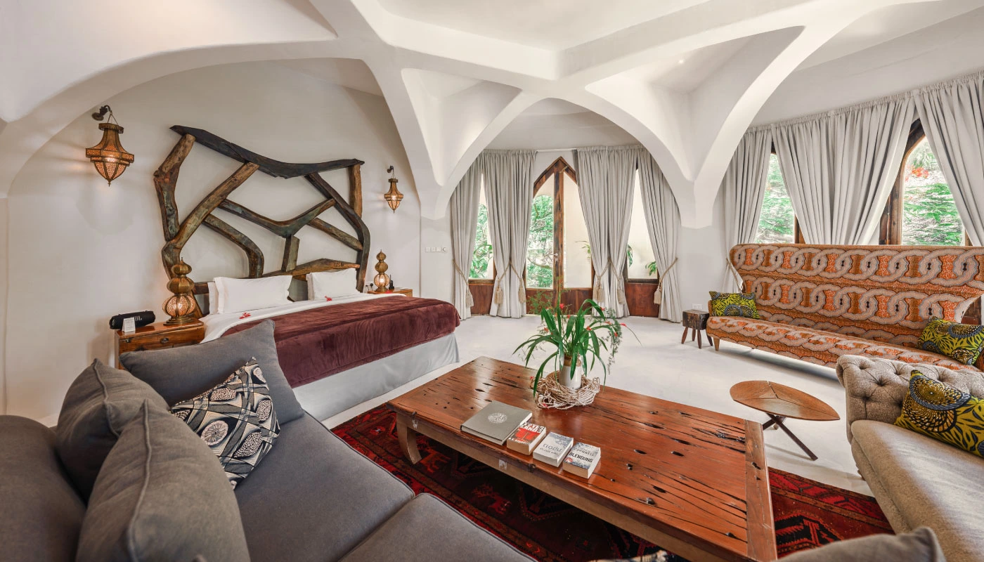 Luxurious bedroom and living area at Mbingu Villa in Xanadu Luxury Villas & Retreat, Zanzibar, featuring an artistic wooden headboard, spacious seating and elegant arched architecture.