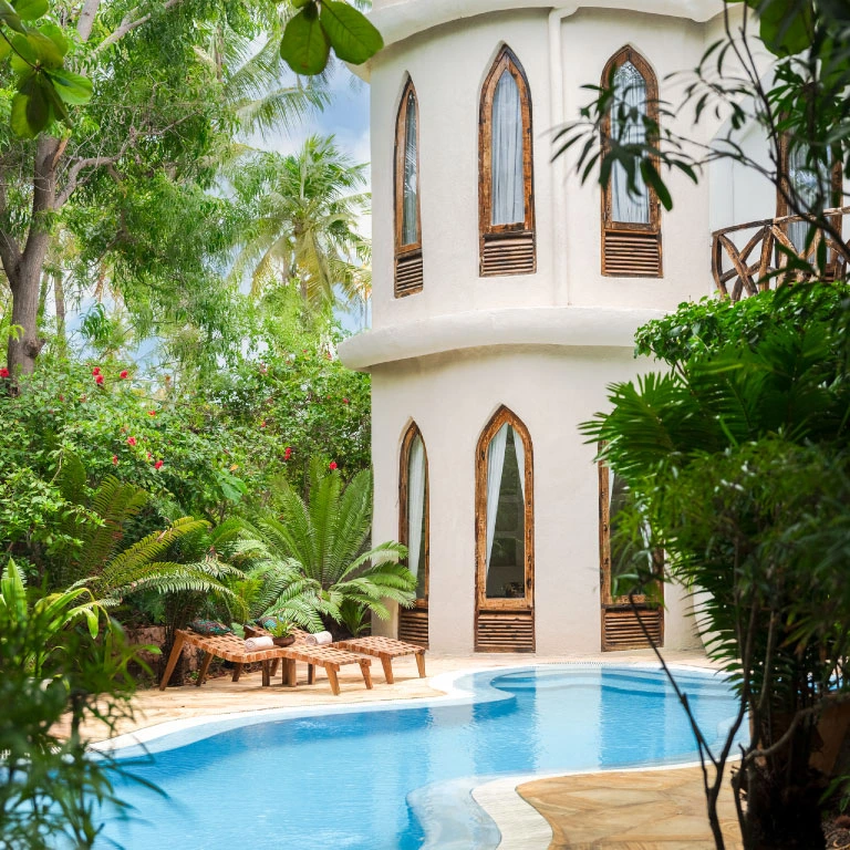 Curved private pool at Mbingu Villa in Xanadu Luxury Villas & Retreat, Zanzibar, surrounded by lush tropical greenery, inviting sun loungers and the villa’s distinctive white architecture.
