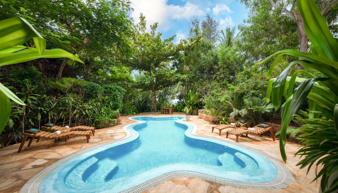 Spacious, curved private pool at Mbingu Villa in Xanadu Luxury Villas & Retreat, Zanzibar, featuring turquoise waters, comfortable sun loungers and lush tropical greenery.