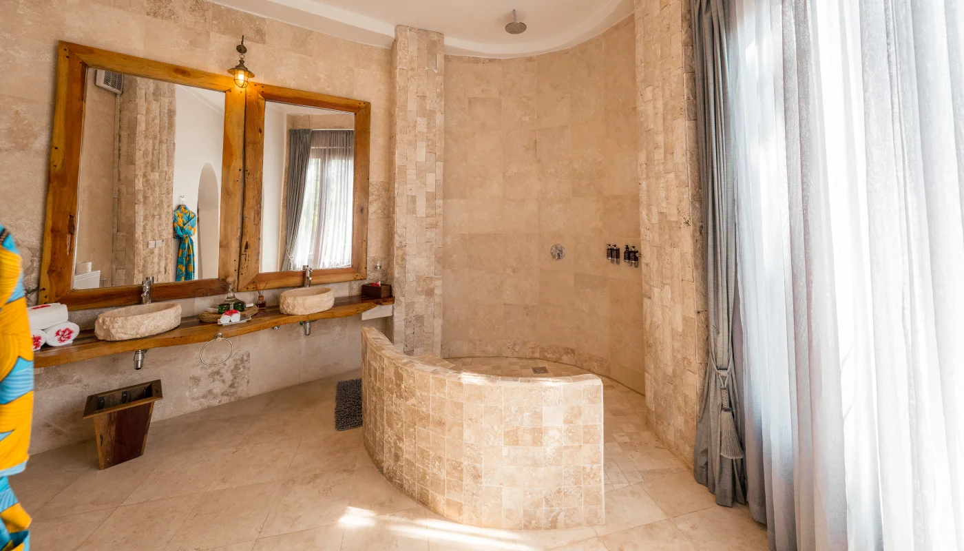 Elegant bathroom at Mlima Villa in Xanadu Luxury Villas & Retreat, Zanzibar, featuring a spacious rainfall shower, double natural stone washbasins and warm wooden accents.