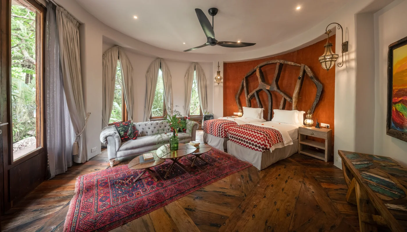 Spacious ground floor bedroom at Mlima Villa in Xanadu Luxury Villas & Retreat, Zanzibar, featuring twin beds, an artistic wooden headboard, a comfortable sofa and warm wooden flooring.