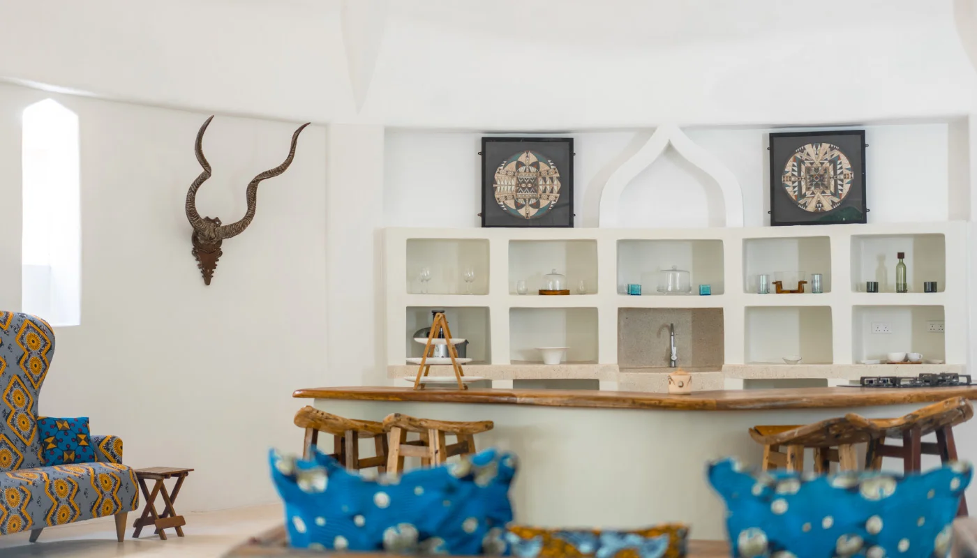 Stylish living area at Mlima Villa in Xanadu Luxury Villas & Retreat, Zanzibar, featuring an adjoining open kitchen, rustic wooden counter, African artwork and colorful seating.