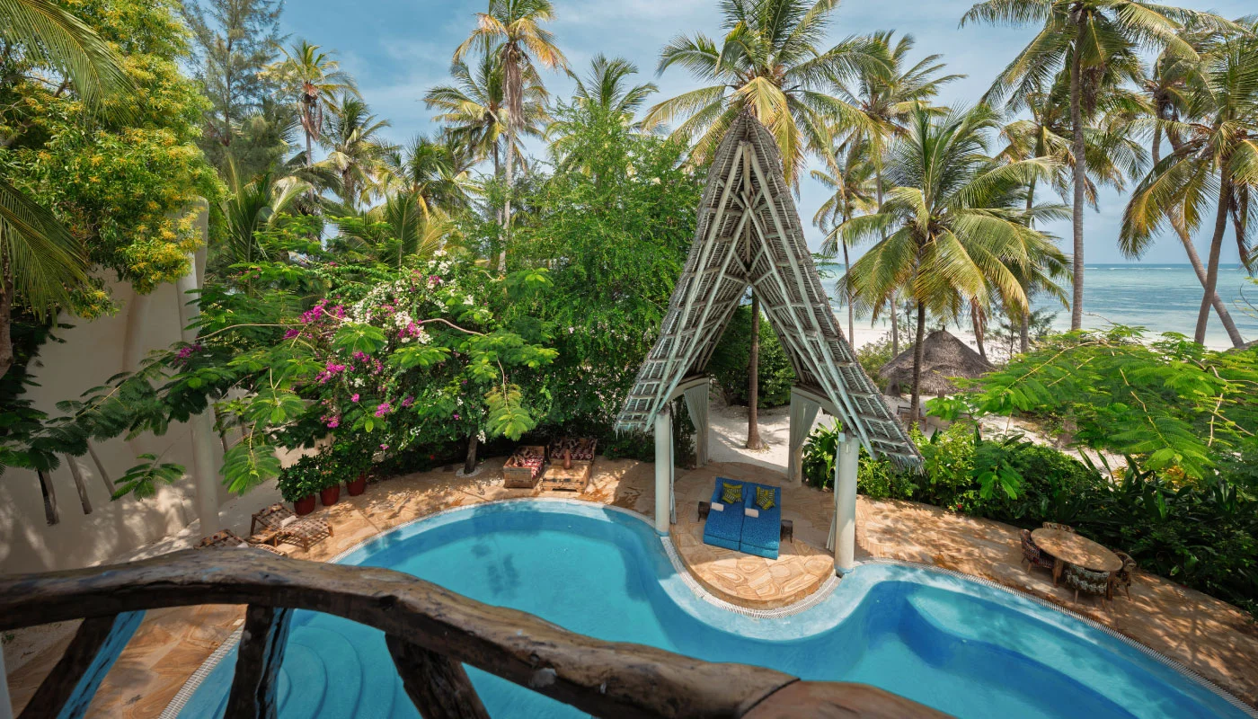 View from the balcony of Nyota Villa at Xanadu Luxury Villas & Retreat, Zanzibar, overlooking the curved private pool, a covered lounge area, tropical palm trees and the Indian Ocean.