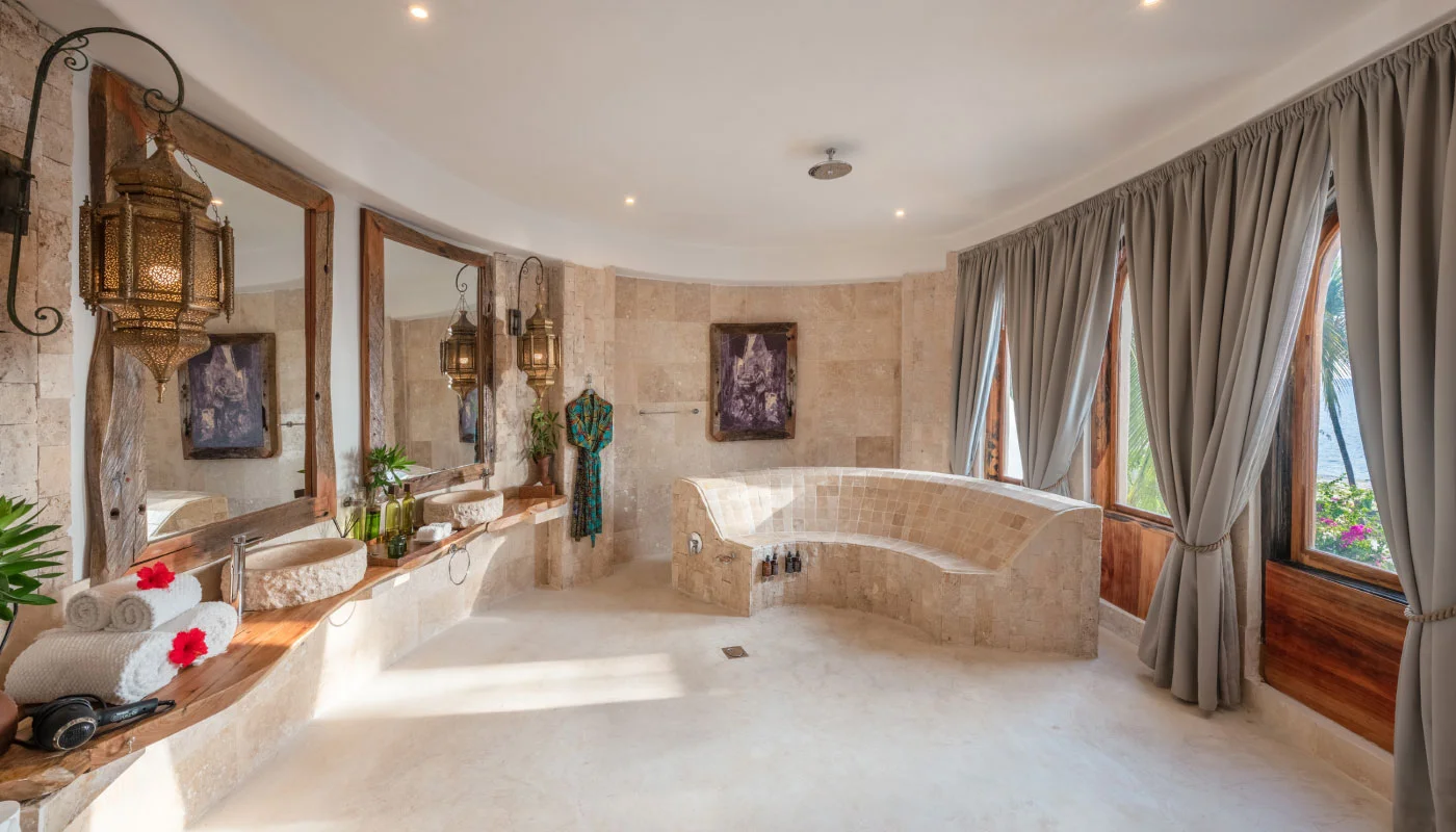 Spacious bathroom at Nyota Villa in Xanadu Luxury Villas & Retreat, Zanzibar, featuring a curved natural stone bench, elegant double washbasins and views of lush tropical greenery.