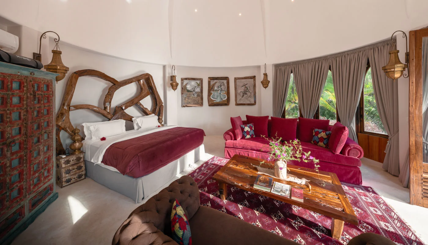 Elegant first floor bedroom at Nyota Villa in Xanadu Luxury Villas & Retreat, Zanzibar, featuring an artistic wooden headboard, a red velvet sofa and a cozy living area.