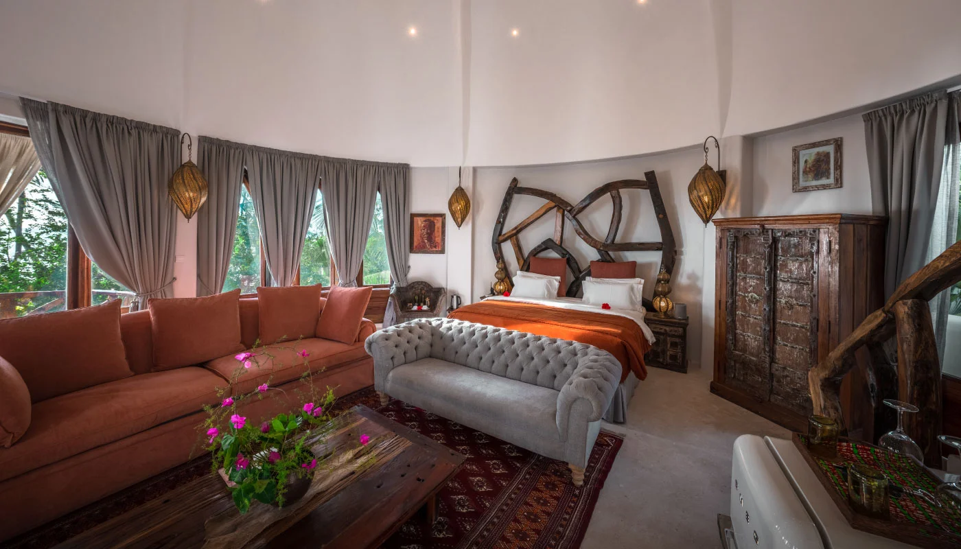 Spacious second floor bedroom at Nyota Villa in Xanadu Luxury Villas & Retreat, Zanzibar, featuring an artistic wooden headboard, comfortable sofas and elegant natural wood furnishings.