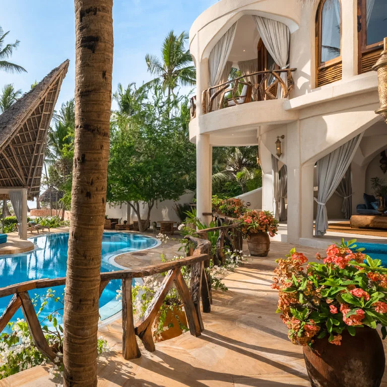 Sunlit terrace at Nyota Villa in Xanadu Luxury Villas & Retreat, Zanzibar, featuring a curved private pool, rustic wooden railings, flowering plants and elegant villa architecture.