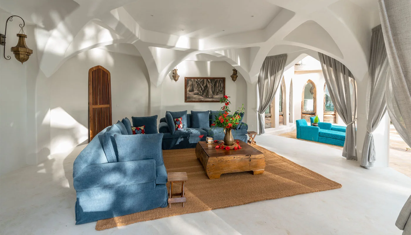 Light-filled lounge area at Nyota Villa in Xanadu Luxury Villas & Retreat, Zanzibar, featuring spacious blue sofas, elegant arches and open access to the pool terrace.