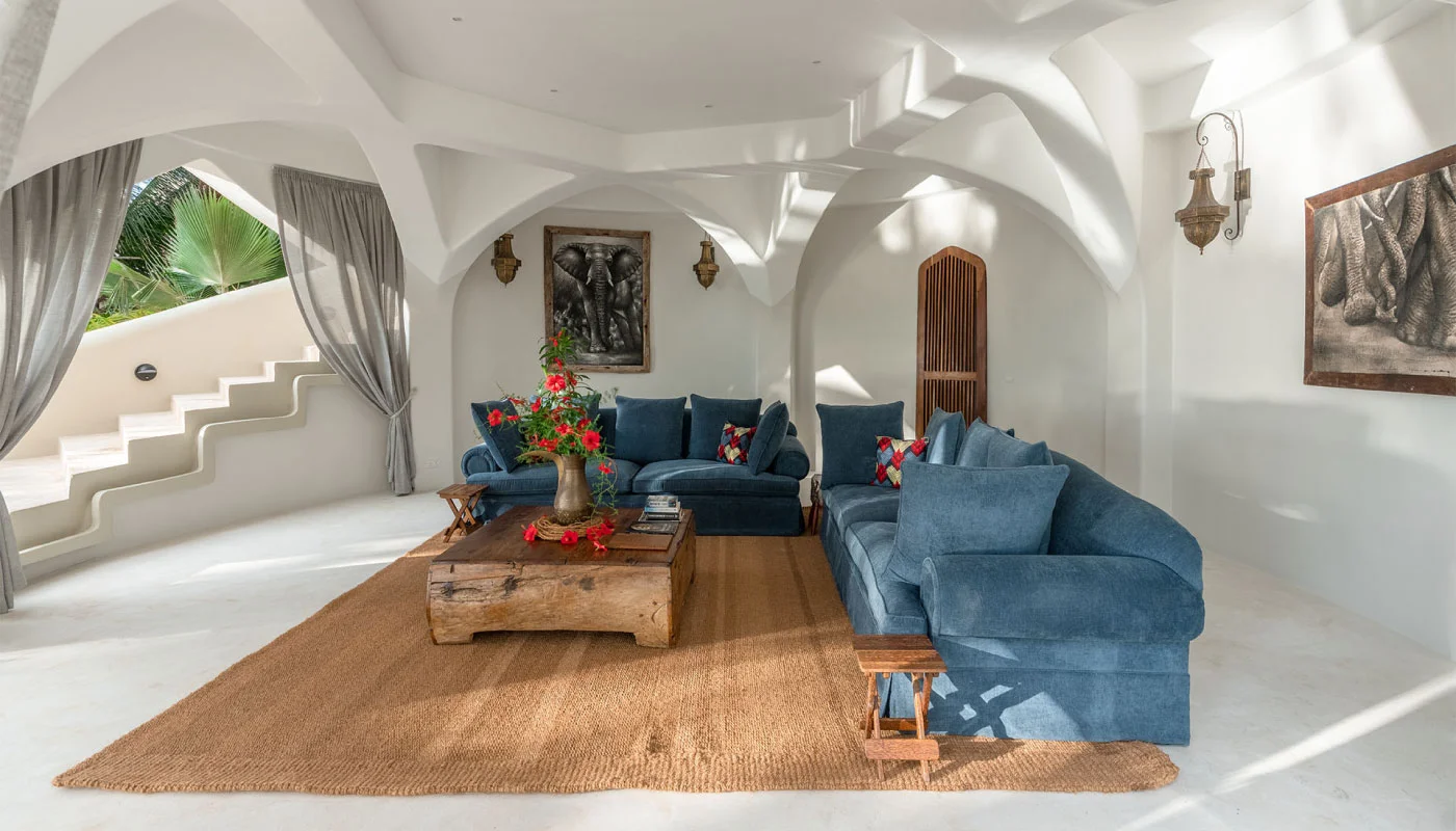 Elegant lounge area at Nyota Villa in Xanadu Luxury Villas & Retreat, Zanzibar, featuring blue sofas, a rustic wooden coffee table, African artwork and graceful arched architecture.