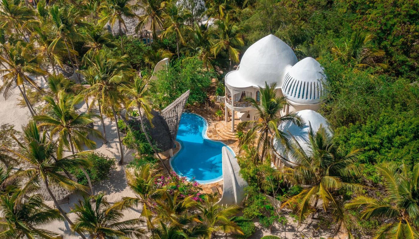Stunning aerial view of Nyota Villa at Xanadu Luxury Villas & Retreat, Zanzibar, featuring distinctive white domed architecture, a curved private pool and lush palm trees near the sandy beach.